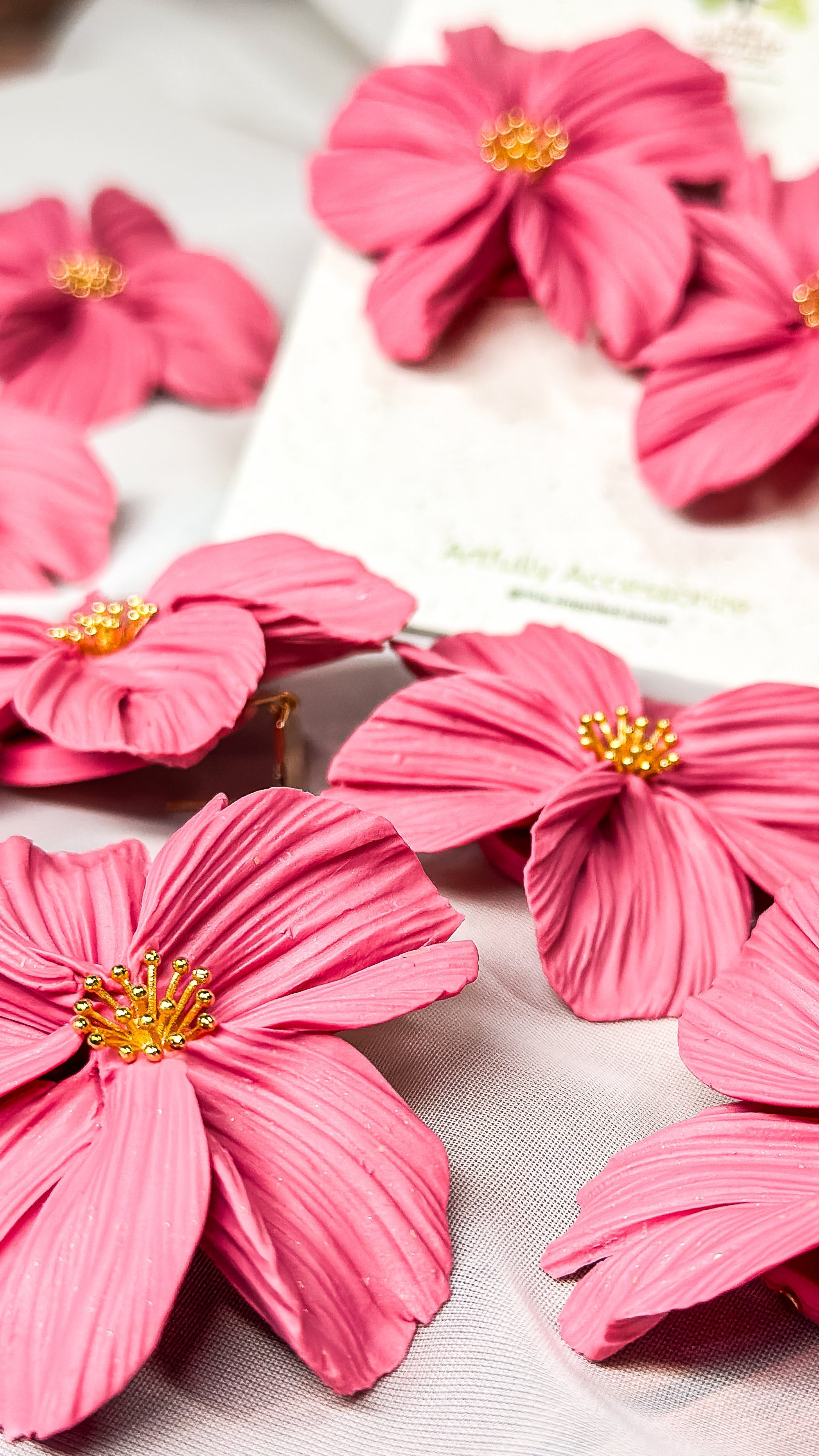 A collection of bubblegum pink floral earrings handcrafted from polymer clay, featuring delicate petal detailing and gold bead centers. February 2025 release.