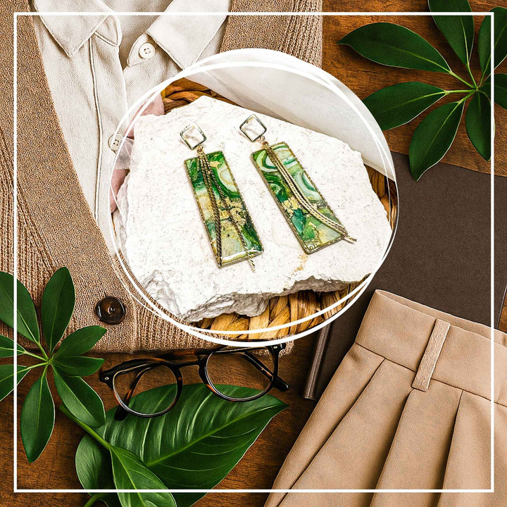 The Dappled Wood's Athena green and gold statement earrings from the Gilded Grove Collection, styled with a pleated skirt, knit cardigan, glasses, greenery, and a journal for a plant-loving professional look.