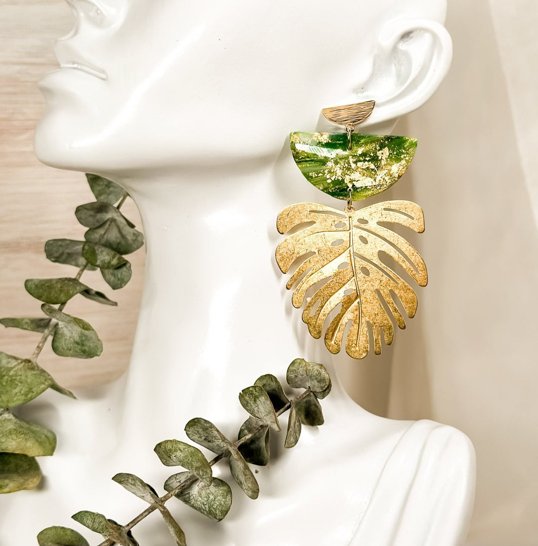 The Dappled Wood's Isolde green and gold leaf statement earrings from the Gilded Grove Collection, displayed on a white mannequin with eucalyptus styling.