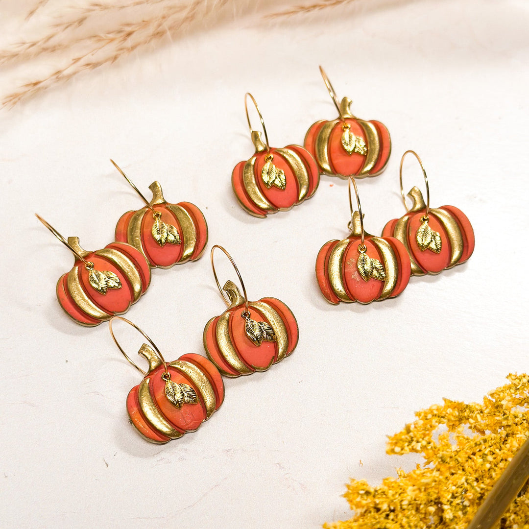 A set of handcrafted polymer clay pumpkin earrings with gold leaf charms from The Dappled Wood’s It’s Fall Y’all 2024 collection.