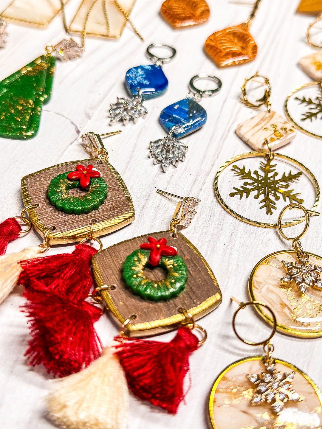 A festive variety of handcrafted polymer clay holiday earrings—wreaths, snowflakes, and tassels—from The Dappled Wood’s Holidays 2024 Winter jewelry collection.