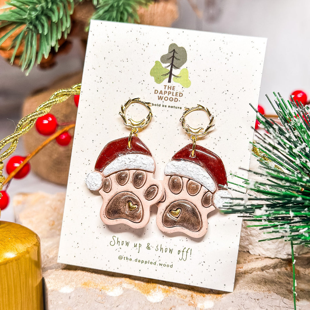 Handcrafted cream pawprint earrings with Santa hats from The Dappled Wood’s Pawliday Fun 2024 collection.