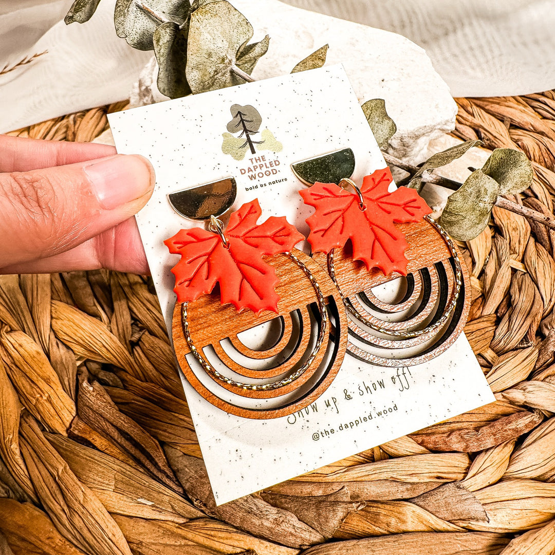 Burnt orange polymer clay maple leaves layered over circular real wood charms