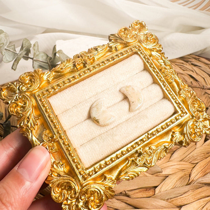 Close-up of Aylin ivory faux stone crescent moon studs in a gold display frame