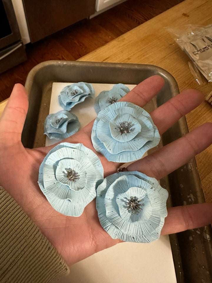 Baby blue circular floral statement stud earrings by The Dappled Wood shown in hand for scale.