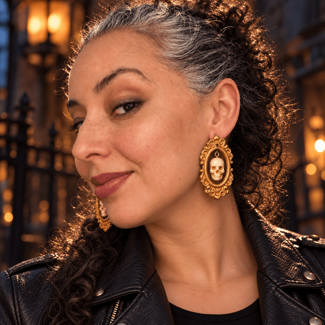 Model wearing Drusilla ivory skull earrings in ornate gold frames with a black jacket.