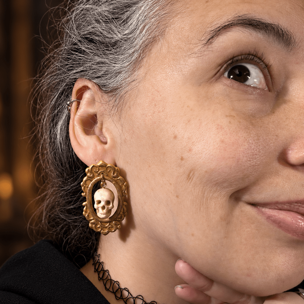 Model wearing Drusilla antique gold framed skull statement earrings