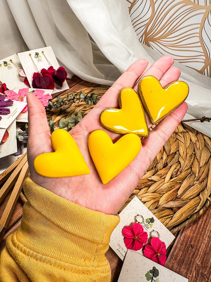 Extra large yellow puffy heart earrings by The Dappled Wood shown in hand for scale.