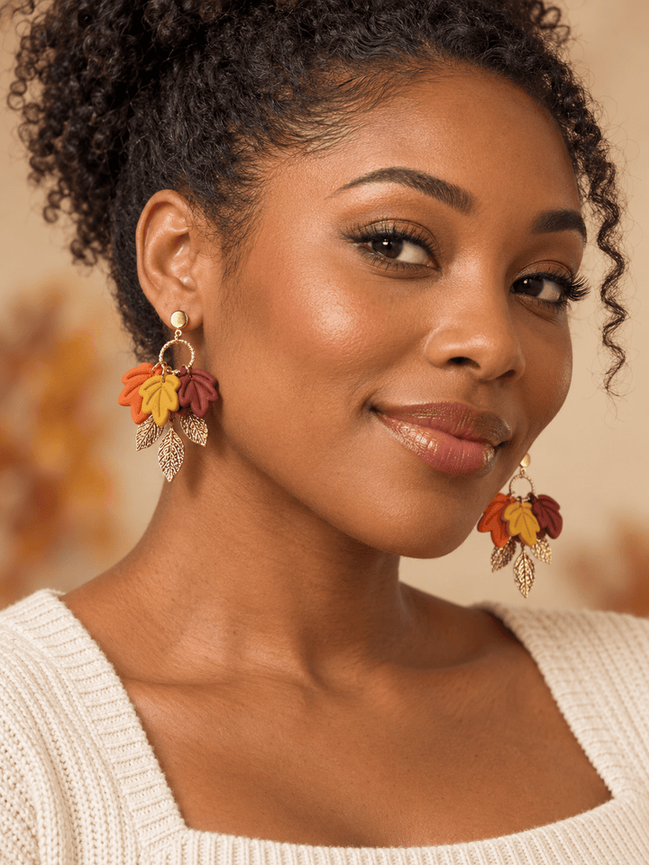 Black woman wearing Fallon Autumn Leaf Earrings by The Dappled Wood with burgundy, mustard yellow, burnt orange, and gold leaves.