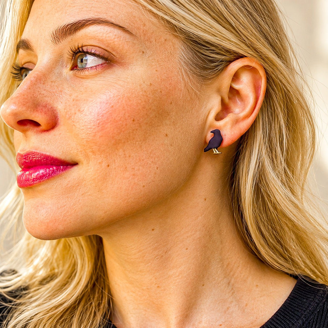 Model wearing black raven Halloween stud earrings with small gold details