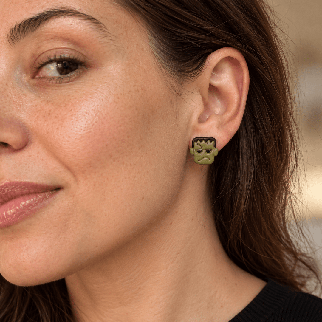 Model wearing olive green Frankenstein Halloween stud earrings with black hair and stitched forehead details