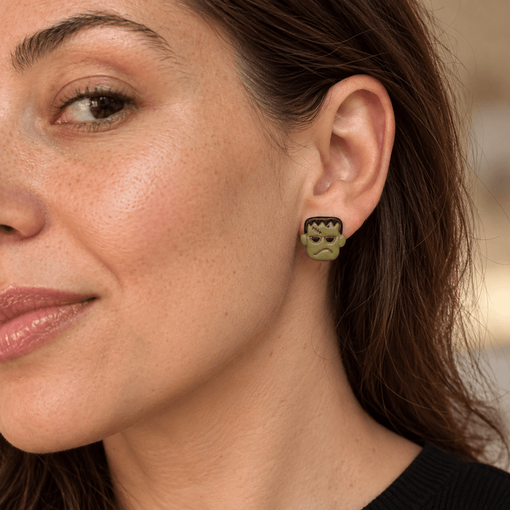 Model wearing olive green Frankenstein Halloween stud earrings with black hair and stitched forehead details