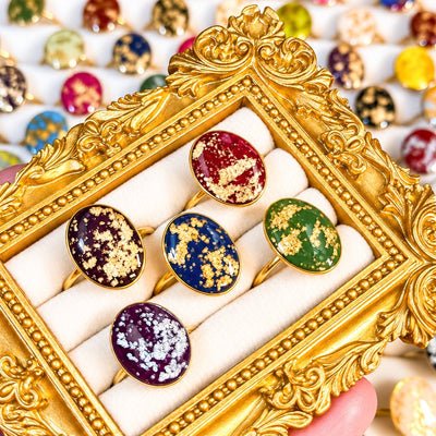 Five Gemma adjustable faux stone statement rings in jewel-tone colors displayed in an ornate gold frame