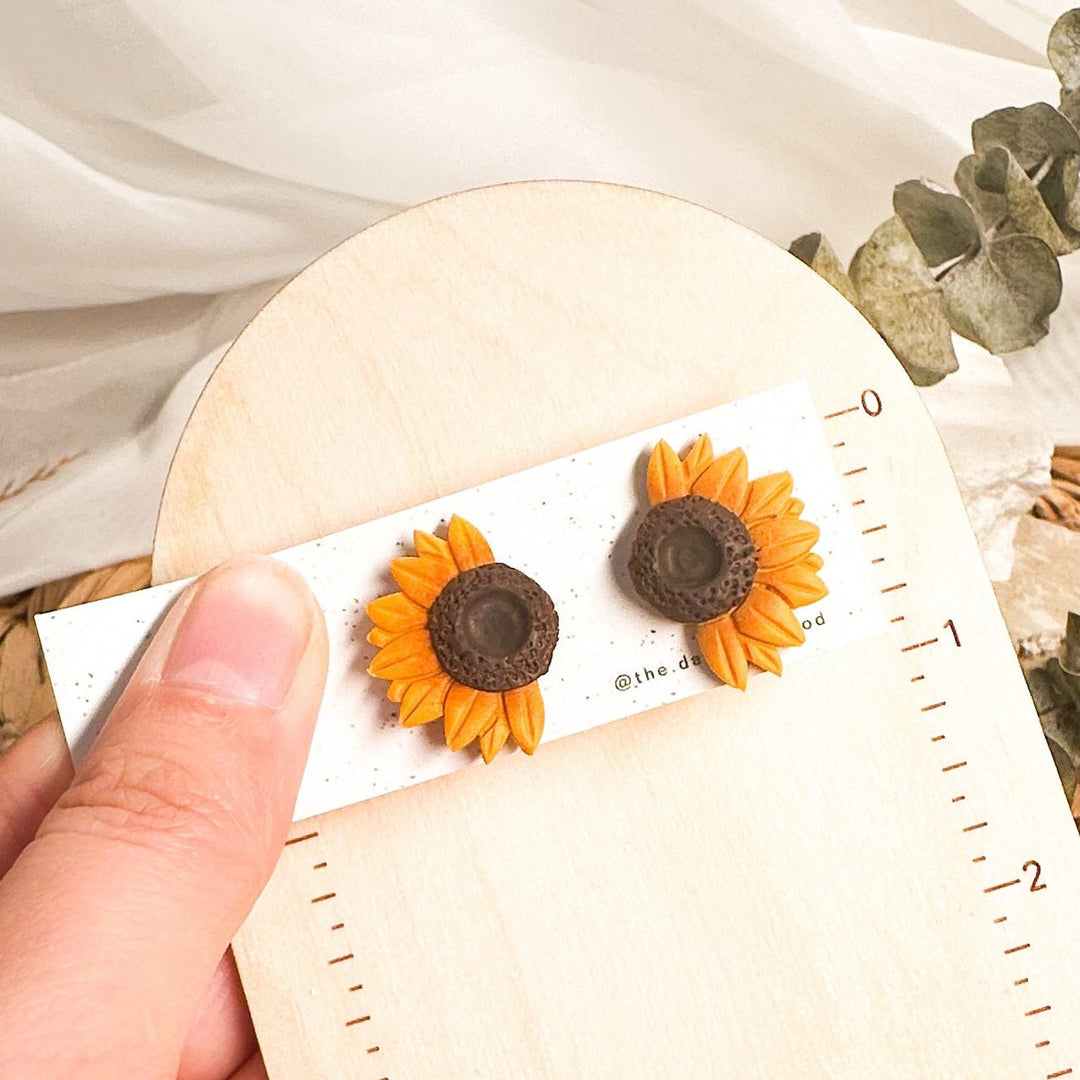 Jean half sunflower stud earrings on a card beside an inch ruler showing approximately 1 inch height