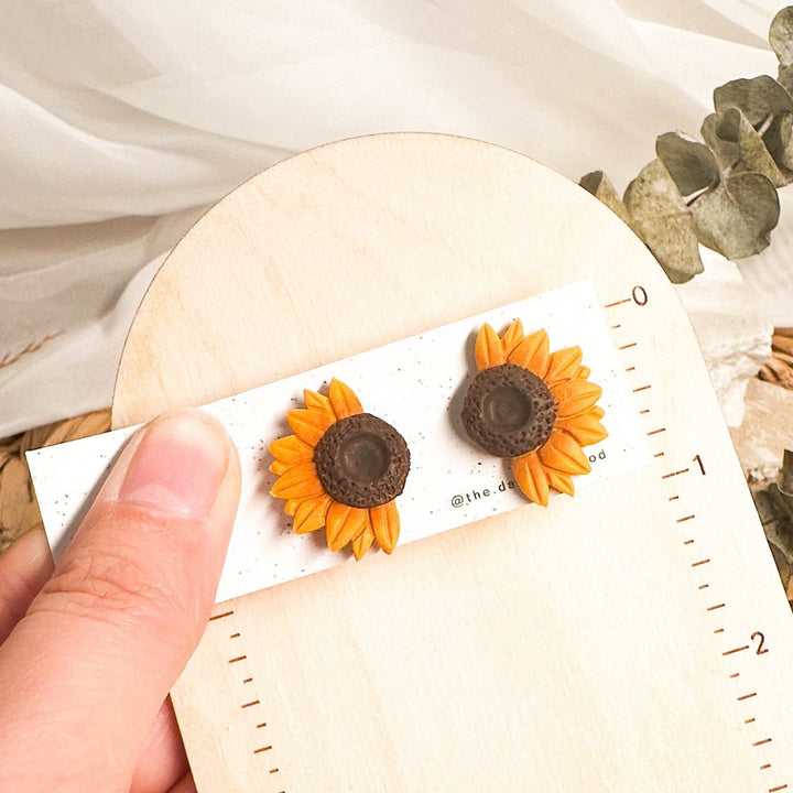 Jean half sunflower stud earrings on a card beside an inch ruler showing approximately 1 inch height
