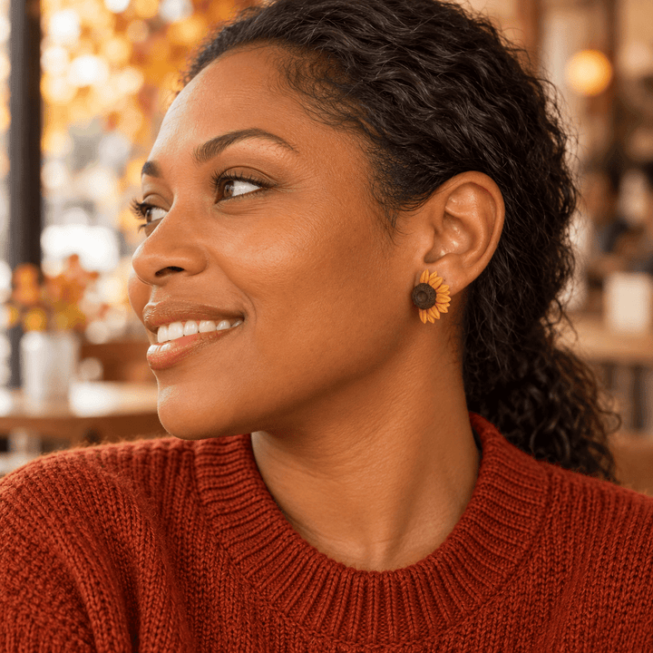 Model in a rust sweater wearing Jean sunflower stud earrings in an autumn cafe