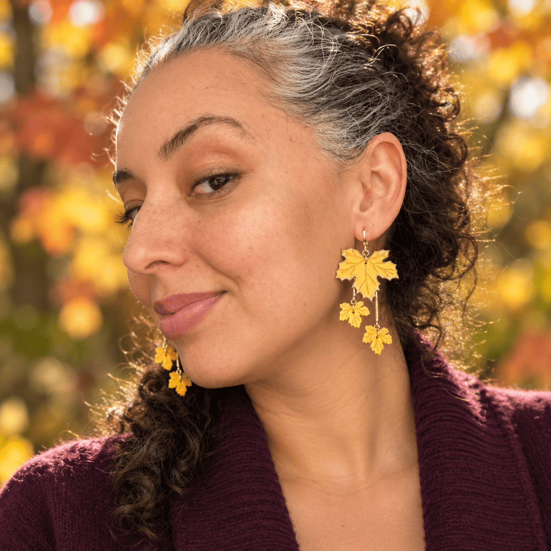 Model wearing Laurel tiered maple leaf earrings in golden yellow outdoors in autumn