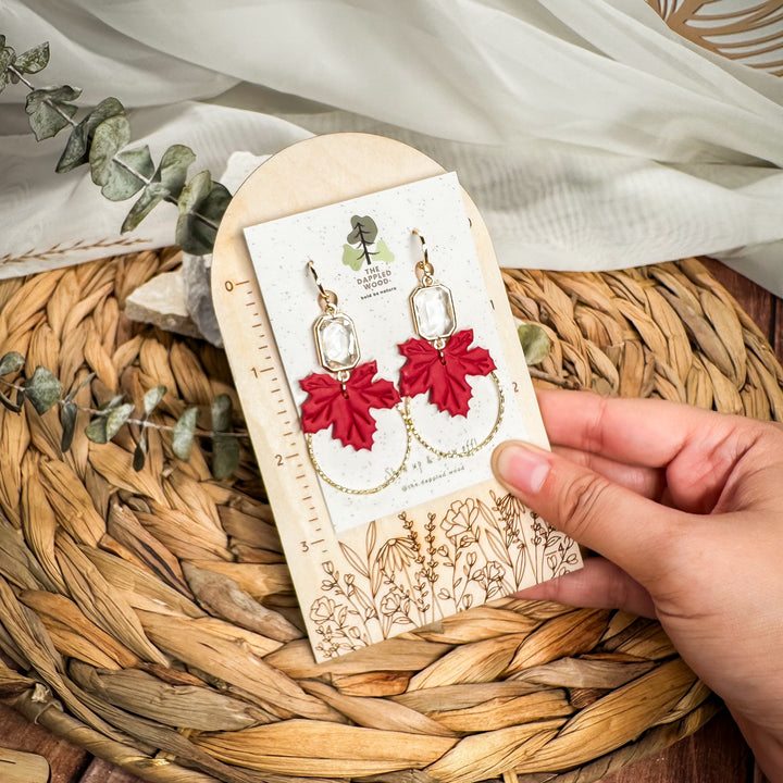 Lucinda maple leaf earrings held on a measurement card showing their statement length