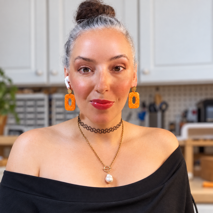 Model wearing Luella alligator-textured statement earrings in Pumpkin Orange by The Dappled Wood.