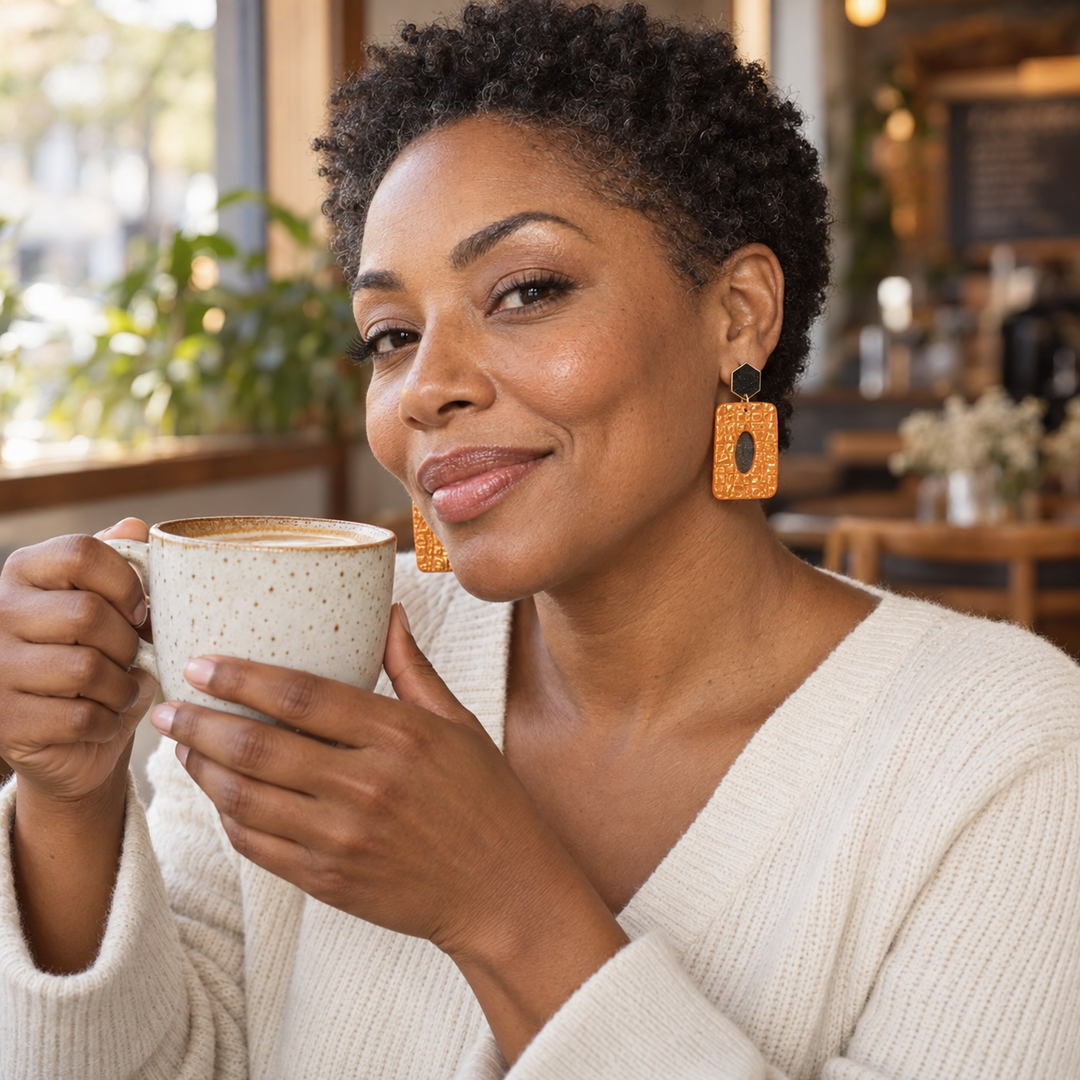 Black woman enjoying coffee while wearing Luella alligator-textured statement earrings in Pumpkin Orange by The Dappled Wood.