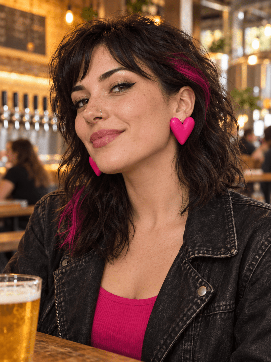 Woman in an alt-rock outfit wearing fuchsia Mabel extra large puffy heart earrings by The Dappled Wood at a brewery.
