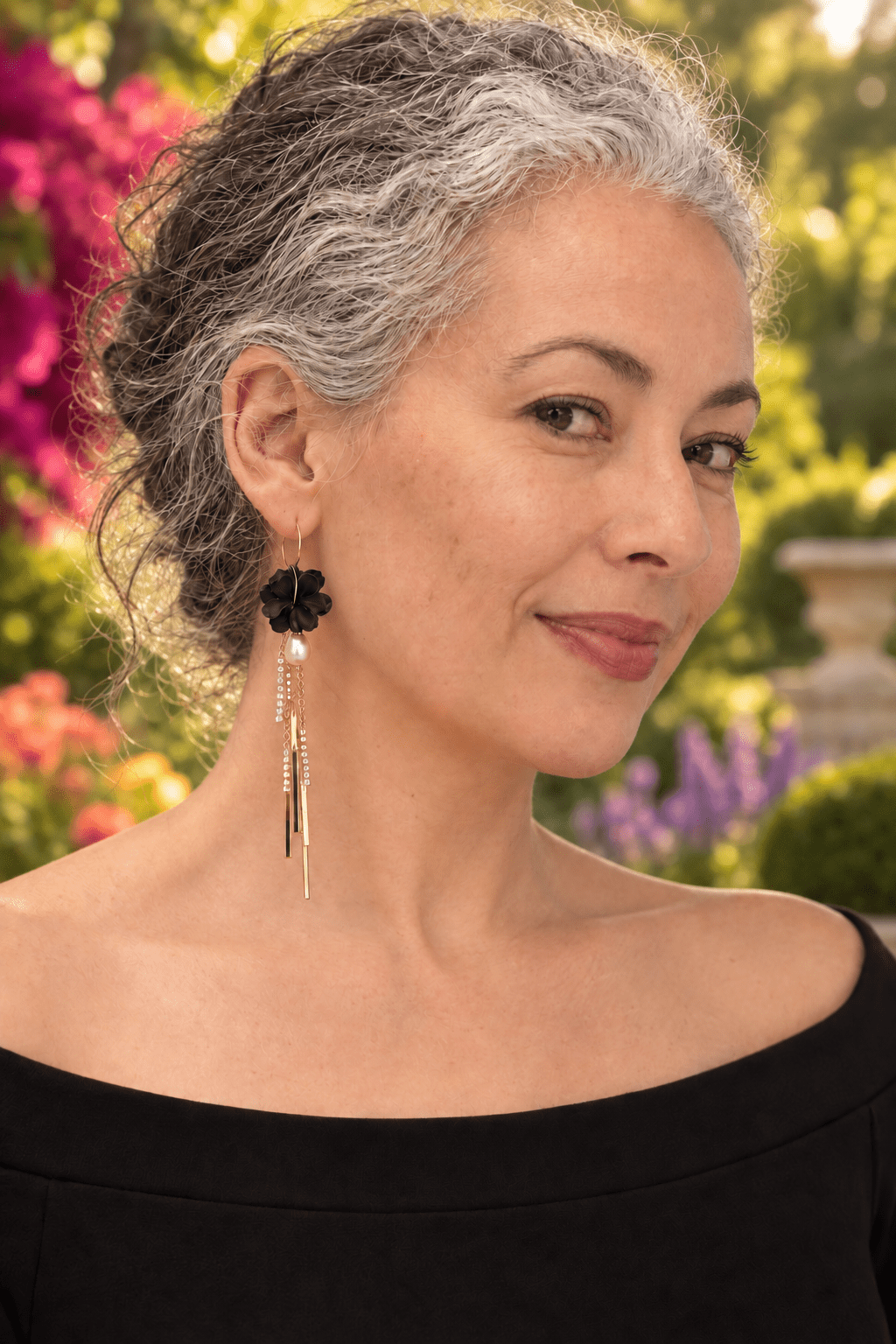 Woman wearing black Martiza long tassel and pearl flower earrings by The Dappled Wood in a colorful garden.