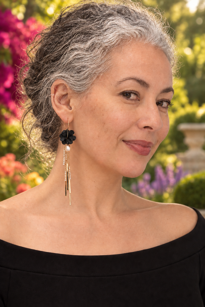 Woman wearing black Martiza long tassel and pearl flower earrings by The Dappled Wood in a colorful garden.