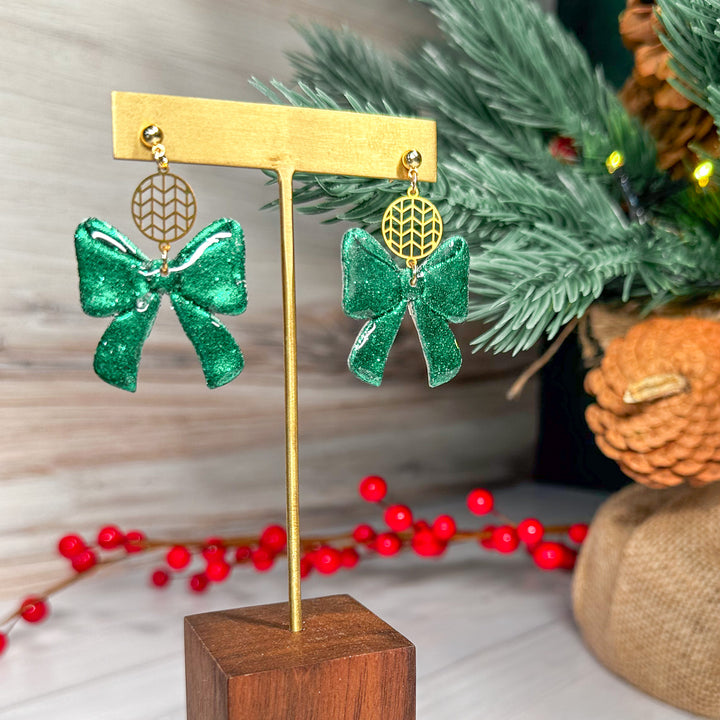 The Dappled Wood Ho Ho Bows earrings in Fir Green, designed with a deep, forest-toned polymer clay bow. A playful holiday earring inspired by Christmas trees and festive decor.