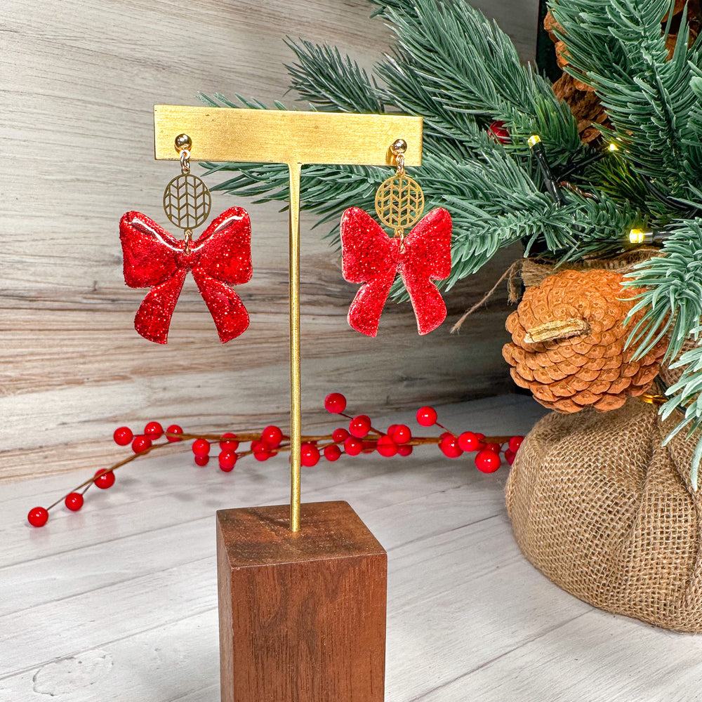 The Dappled Wood Ho Ho Bows earrings in Santa Red, handcrafted polymer clay bows with a bold holiday shimmer. A festive statement piece perfect for Christmas celebrations.