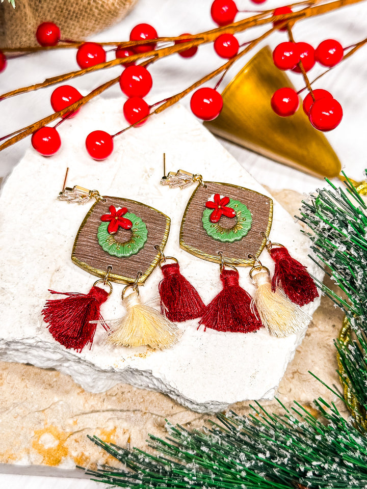 The Dappled Wood Holly Jolly sculpted wreath earrings with red and white tassels on CZ gold posts, adding holiday charm to any look.