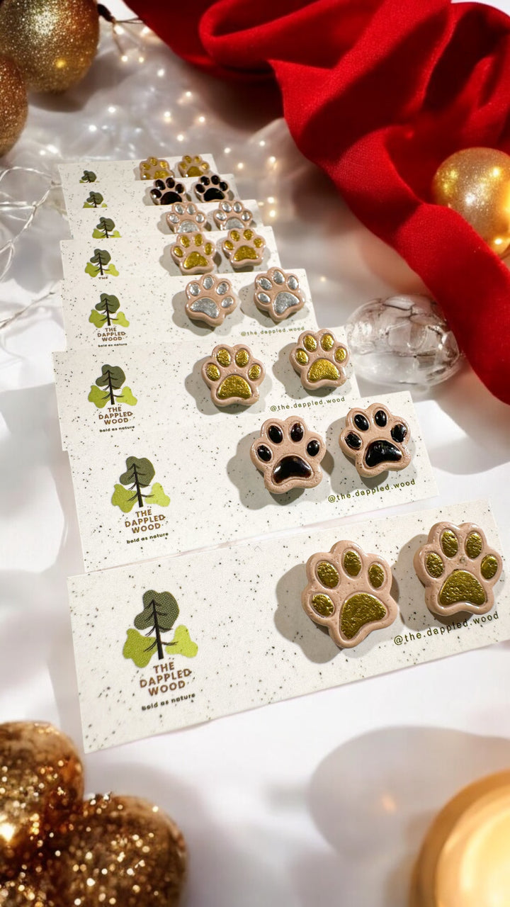 The Dappled Wood Santa Paws stud earrings, handcrafted from polymer clay in a paw print design with festive holiday colors. Featuring a lightweight and hypoallergenic design, perfect for pet lovers celebrating the season.