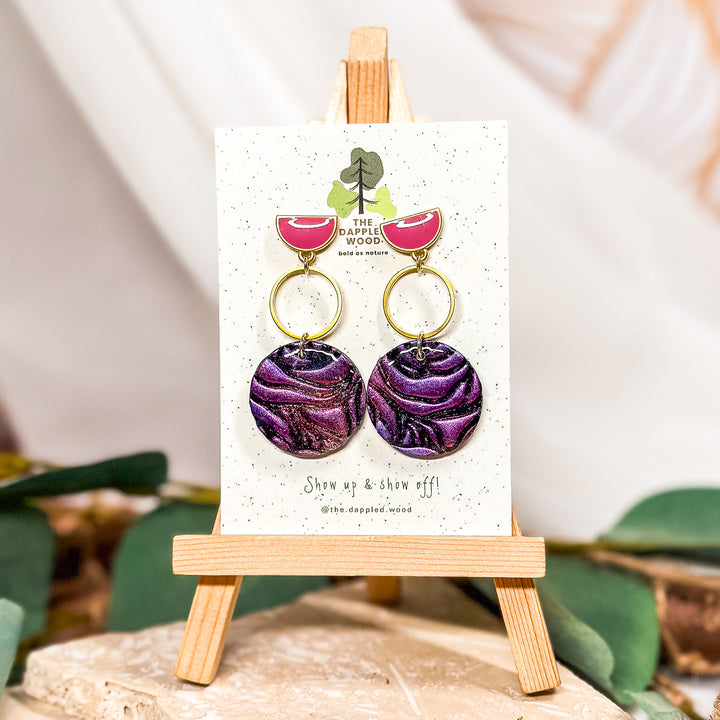 The Dappled Wood Carla rose-embossed circle earrings, featuring hand-sculpted deep purple polymer clay roses on pink half-moon posts. A bold yet feminine statement for New Year's celebrations and beyond.