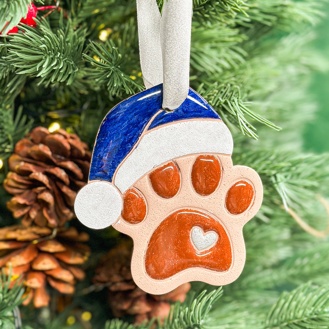 Festive paw print ornament with a blue Santa hat, a unique holiday decoration. 2025.