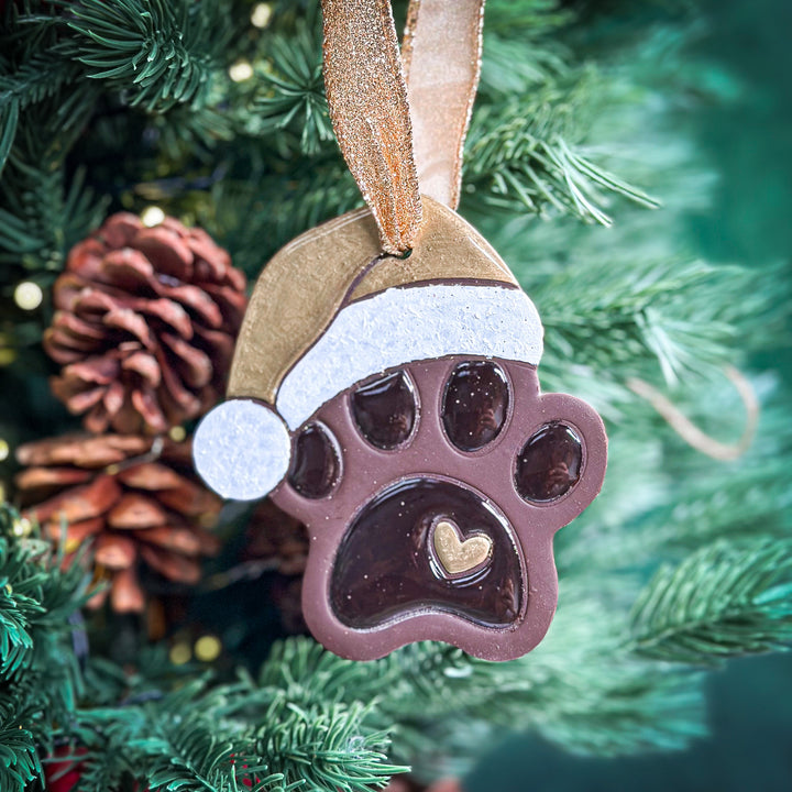 Handmade paw print ornament with a gold Santa hat, ideal for holiday decor. 2025.