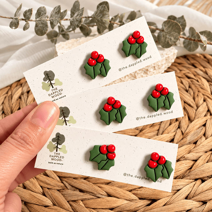 Agnes green holly leaf stud earrings with glossy red berries on cards.