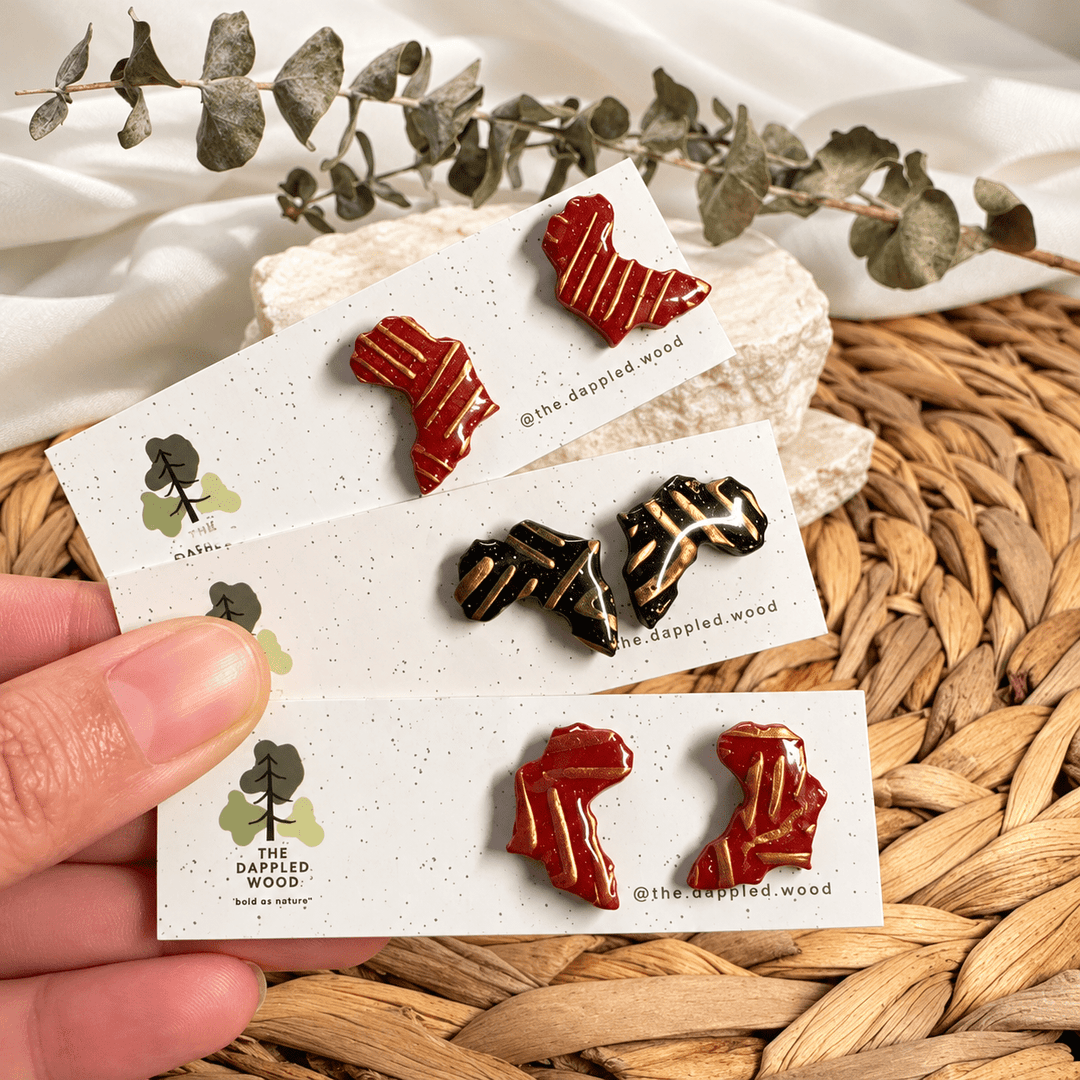 Ayana brick-red and black Africa stud earrings with raised gold linework on display cards.