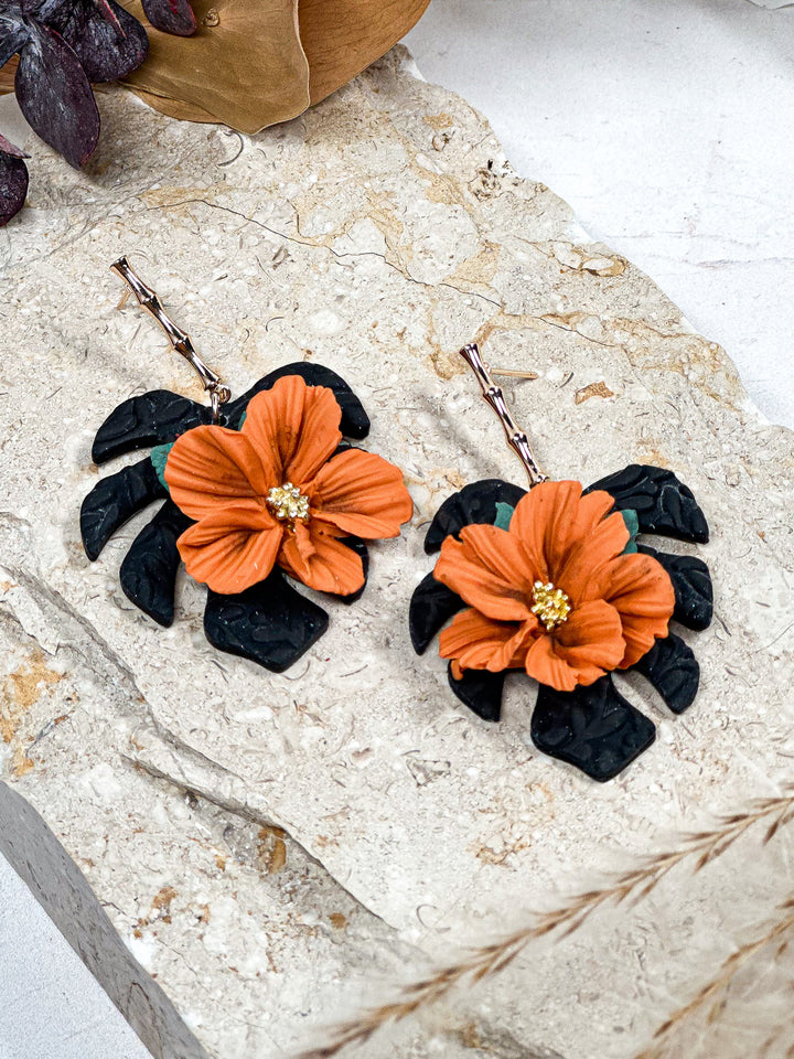 Black monstera earrings with an orange flower charm, nature-inspired lightweight earrings by The Dappled Wood.