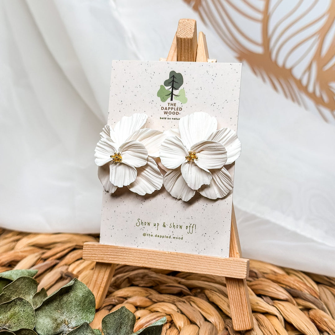 Blossom double stacked petal statement stud earrings from The Dappled Wood displayed on a branded card with textured white flower petals and gold center details.