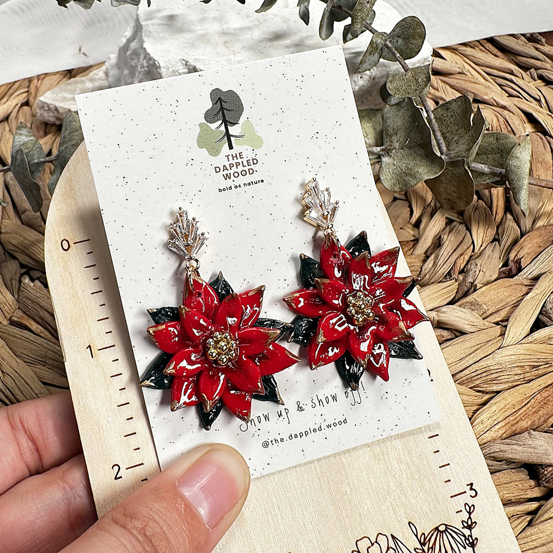 Original handmade Carmela poinsettia earrings in glossy red and dark green polymer clay with gold accents and crystal fan posts