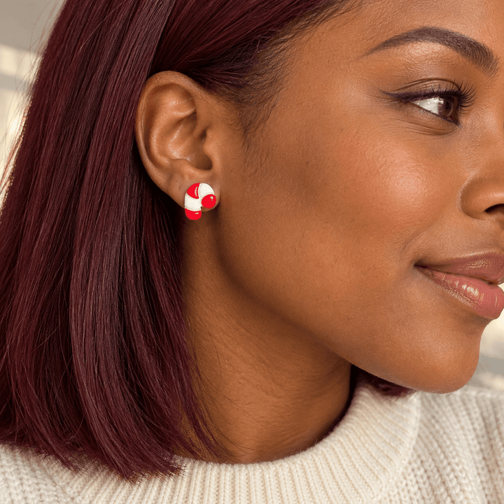 AI-generated styling preview of Claudette candy cane studs on a model with deep brown skin and burgundy hair; scale illustrative.