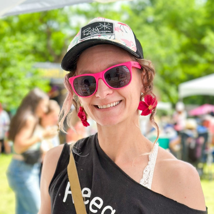 Customer at an outdoor market wearing The Dappled Wood Flora flower earrings in fuchsia.