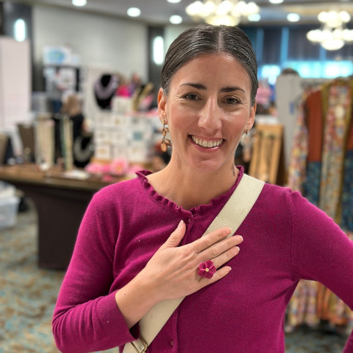 Customer at a market wearing The Dappled Wood Isadora flower earrings and matching flower ring, smiling and posing in a fuchsia sweater.