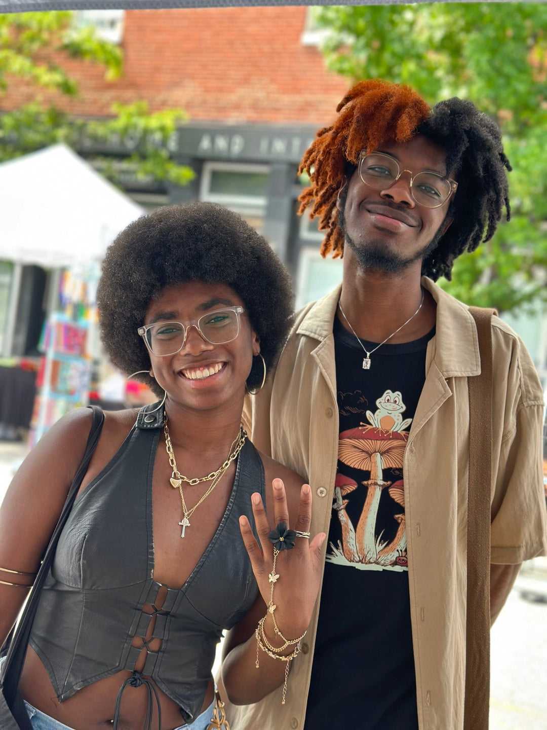 Two customers smiling at an outdoor market, one showcasing The Dappled Wood black Isadora flower ring while wearing a black outfit and layered jewelry.