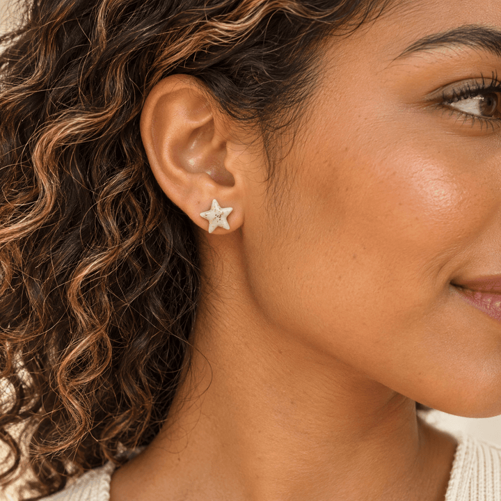 AI-generated styling preview of a model with caramel-highlighted curls wearing an Estelle star stud; scale is illustrative