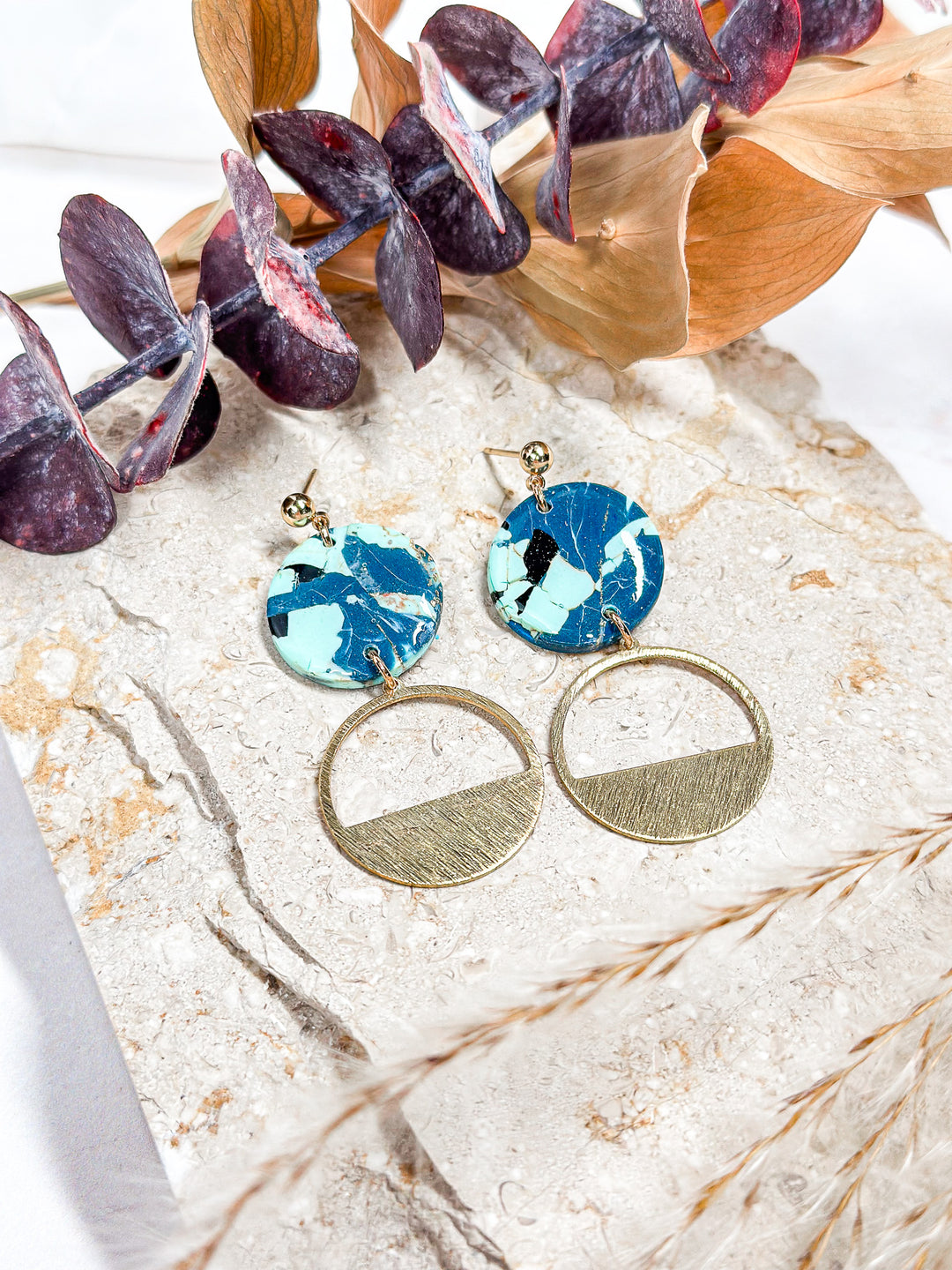 The Dappled Wood’s Spooky Skies earrings with a circular gold charm, featuring a marbled blue and black design for a bold fall statement.