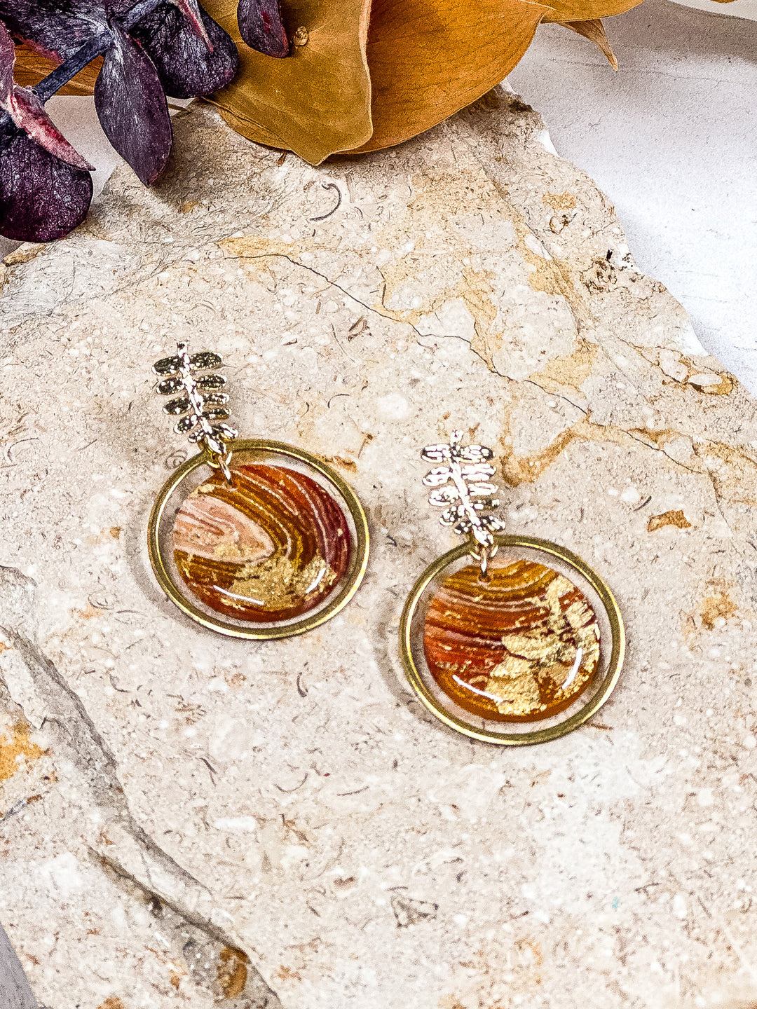 The Dappled Wood’s Traces of Tangerine nature-inspired earrings with a circular design, gold ring, and leaf branch post. Lightweight polymer clay jewelry, perfect for bold fall looks.