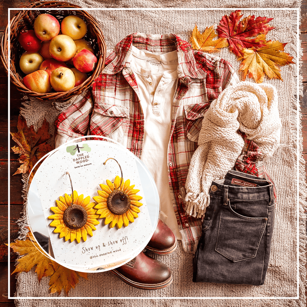Clara handmade sunflower earrings by The Dappled Wood styled in apple picking outfit flatlay with red plaid flannel shirt, cream henley, dark jeans, leather lace-up boots, chunky knit scarf, apples, and fall leaves