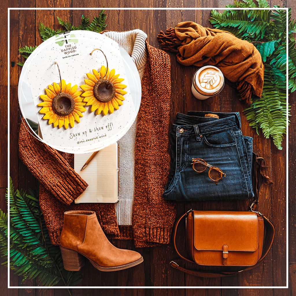 Clara handmade sunflower earrings by The Dappled Wood styled in cozy coffee shop flatlay with rust cardigan, cream turtleneck sweater, dark jeans, suede ankle boots, leather crossbody bag, sunglasses, journal, and latte