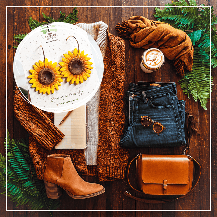 Clara handmade sunflower earrings by The Dappled Wood styled in cozy coffee shop flatlay with rust cardigan, cream turtleneck sweater, dark jeans, suede ankle boots, leather crossbody bag, sunglasses, journal, and latte
