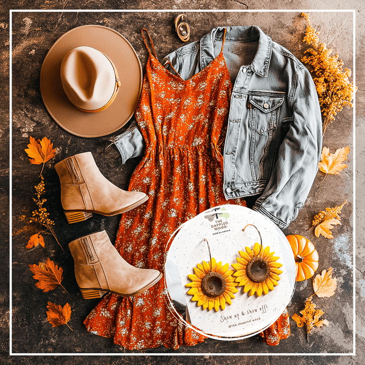 Clara handmade sunflower earrings by The Dappled Wood styled in fall festival flatlay with rust orange floral dress, light denim jacket, tan ankle boots, wide-brim hat, gold jewelry, mini pumpkin, and autumn leaves